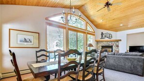 A dining area with a wooden table and chairs, a chandelier, and a fireplace. - Windward Way Retreat House (Steamboat Springs)