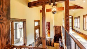 A wooden staircase with a railing, a chandelier, and a view of the outside. - Rocky Fells House (Breckenridge)