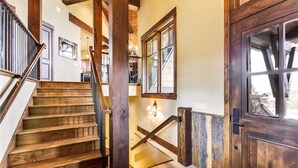 A wooden staircase with a handrail, a door with glass panels, and a wall-mounted light fixture. - Rocky Fells House (Breckenridge)