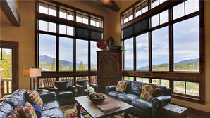 A spacious living room with large windows, a fireplace, leather sofas, and a coffee table. - Rocky Fells House (Breckenridge)