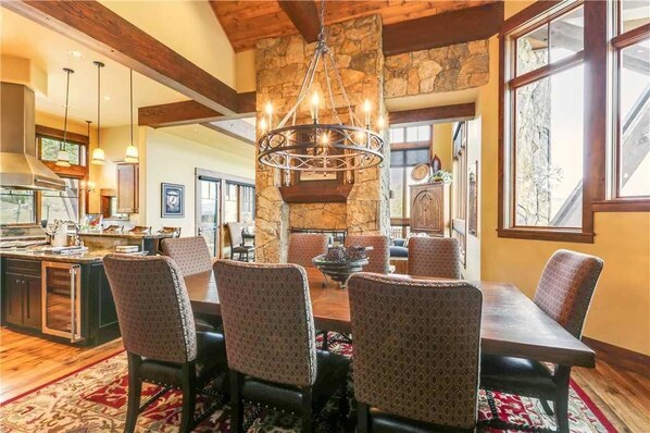 A spacious dining area with a stone fireplace, wooden beams, and a chandelier.