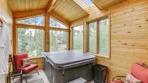 Un intérieur de chalet chaleureux avec un bain à remous, de grandes fenêtres et une vue sur la forêt.
