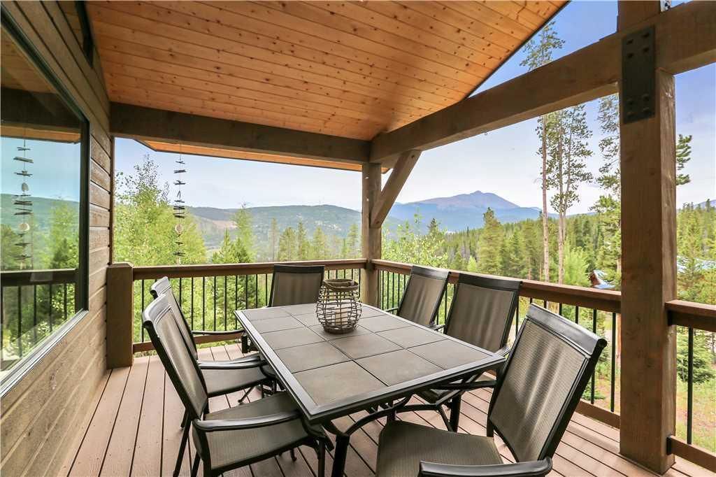 A covered outdoor area with a table and chairs, overlooking a mountainous landscape.