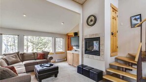 Ein geräumiges Wohnzimmer mit einer großen Eckcouch, einem Kamin, einem Fernseher und einer Treppe.