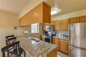 A kitchen with granite countertops, stainless steel appliances, wooden cabinets, and a central island with bar stools.
