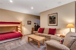 A cozy room with a bunk bed, a sofa, a coffee table, and a lamp. - Pines 99 Town House (Breckenridge)