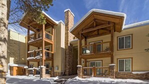 A multi-story building with a stone facade, wooden balconies, and snow on the roof and ground. - Columbine 105 Condo (Breckenridge)