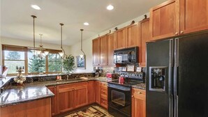 A kitchen with wooden cabinets, granite countertops, a black refrigerator, a microwave, and an oven. - Highland Green 91 Town House (Breckenridge)
