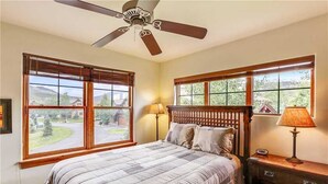 A bedroom with a bed, two windows, a ceiling fan, and a nightstand with a lamp. - Highland Green 91 Town House (Breckenridge)