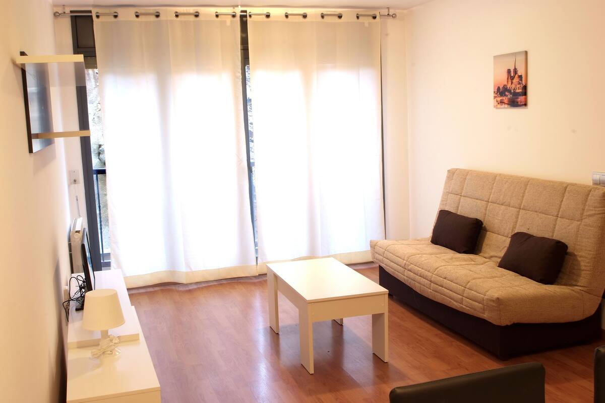 Una sala de estar con un sofá, una mesita y un televisor sobre un mueble.