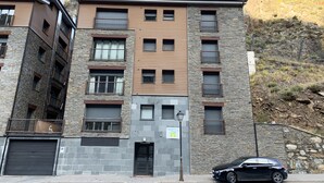 Un edificio de varios pisos con fachada de piedra y numerosas ventanas, con un coche negro estacionado frente a él.