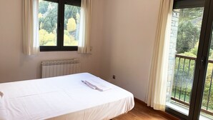 Un dormitorio con cama, ventana, radiador y balcón con vista a árboles.