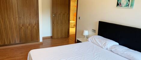 Habitación de hotel con una cama grande, armario de madera y un baño visible a través de una puerta abierta.