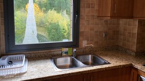 Cocina con un ventanal grande, encimera de granito, pileta de acero inoxidable y muebles de madera.
