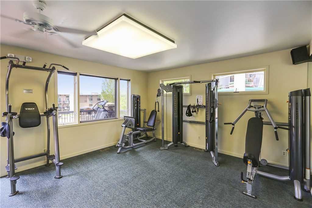 A gym with various exercise equipment, large windows, and a ceiling fan.