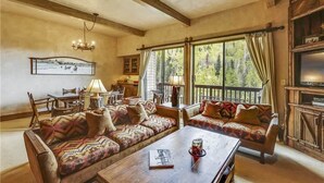 A cozy living room with a wooden ceiling, a large window with curtains, a sofa set, a coffee table, and a television. - Storm Meadows Townhouse 17 Town House (Steamboat Springs)