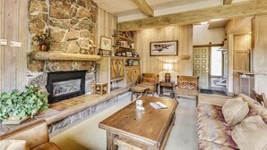 A rustic living room with a stone fireplace, wooden beams, a sofa, and a coffee table. - Storm Meadows Townhouse 17 Town House (Steamboat Springs)