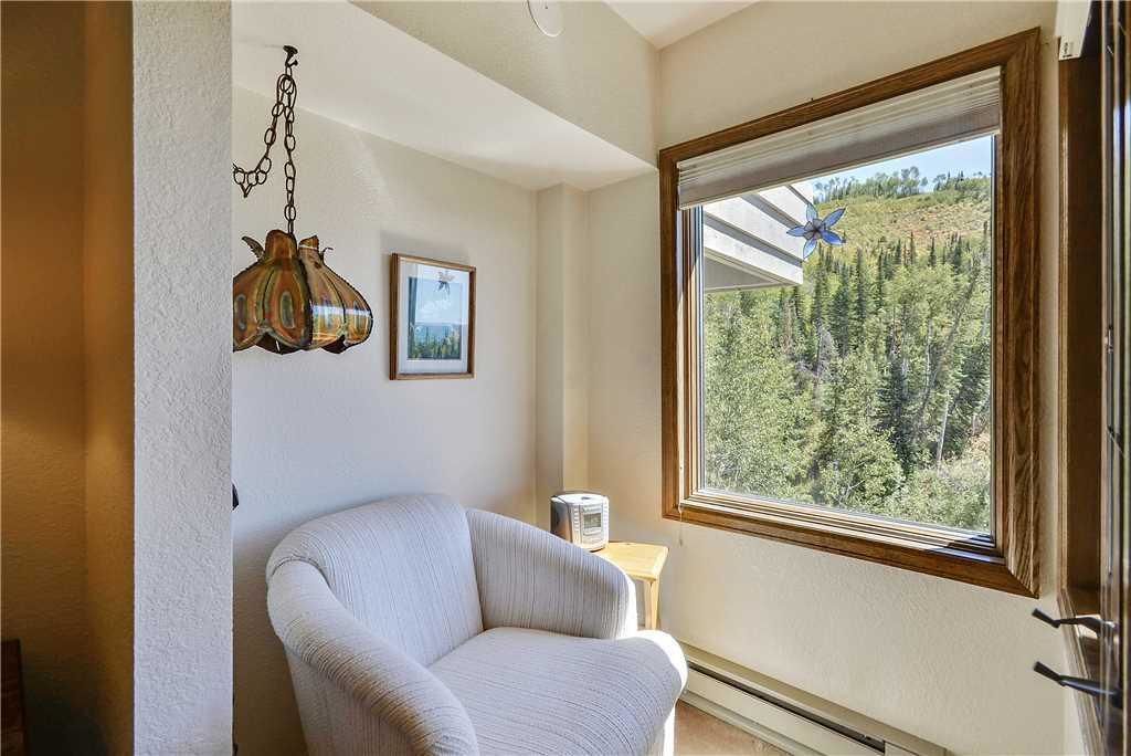 A room with a large window, a chair, a hanging light fixture, and a framed picture on the wall.