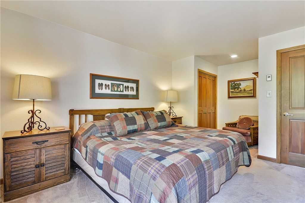 A bedroom with a wooden bed, two bedside tables with lamps, a wooden wardrobe, and a framed picture on the wall.