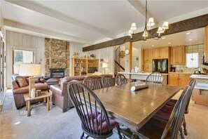 A spacious living room with a fireplace, a dining area with a large wooden table, and a kitchen with wooden cabinets and a built-in oven.