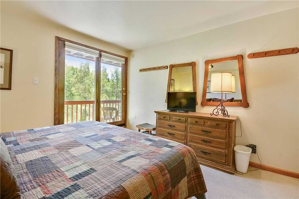 A bedroom with a large bed, a wooden dresser, a television, and a sliding glass door leading to a balcony.