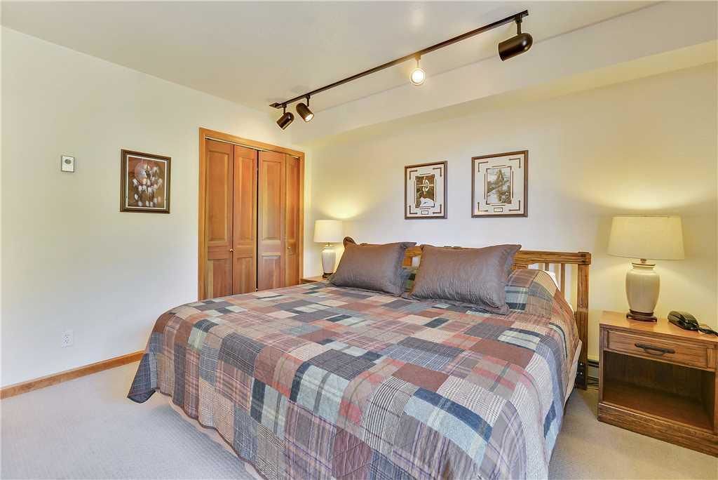 Quarto com uma cama grande, guarda-roupa de madeira, duas luminárias de cabeceira e quadros nas paredes.