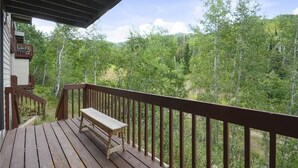 A wooden deck with a bench, overlooking a forested area.