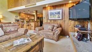 A spacious living area with wooden paneling, a sofa, a coffee table with a magazine, and a television on the right.