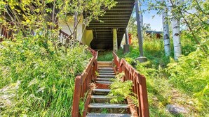 A wooden staircase leading up to a building under a bridge, surrounded by lush greenery. - Storm Meadows Townhouse 24 Town House (Steamboat Springs)