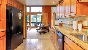 A kitchen with wooden cabinets, a black refrigerator, a dining area with a table and chairs, and a view of the outdoors through large windows. - Storm Meadows Townhouse 24 Town House (Steamboat Springs)