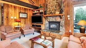 A cozy living room with wooden walls, a stone fireplace, and a television. - Storm Meadows Townhouse 24 Town House (Steamboat Springs)