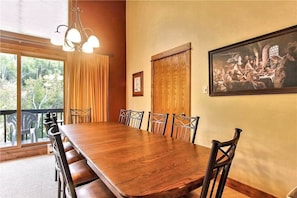 A dining room with a long wooden table, chairs, a chandelier, and a painting on the wall.