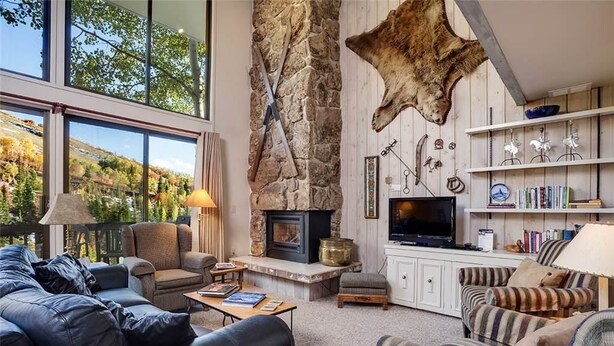 A cozy living room with a stone fireplace, leather sofas, and a bookshelf filled with books and decorative items. - Storm Meadows Townhouse 4 Town House (Steamboat Springs)