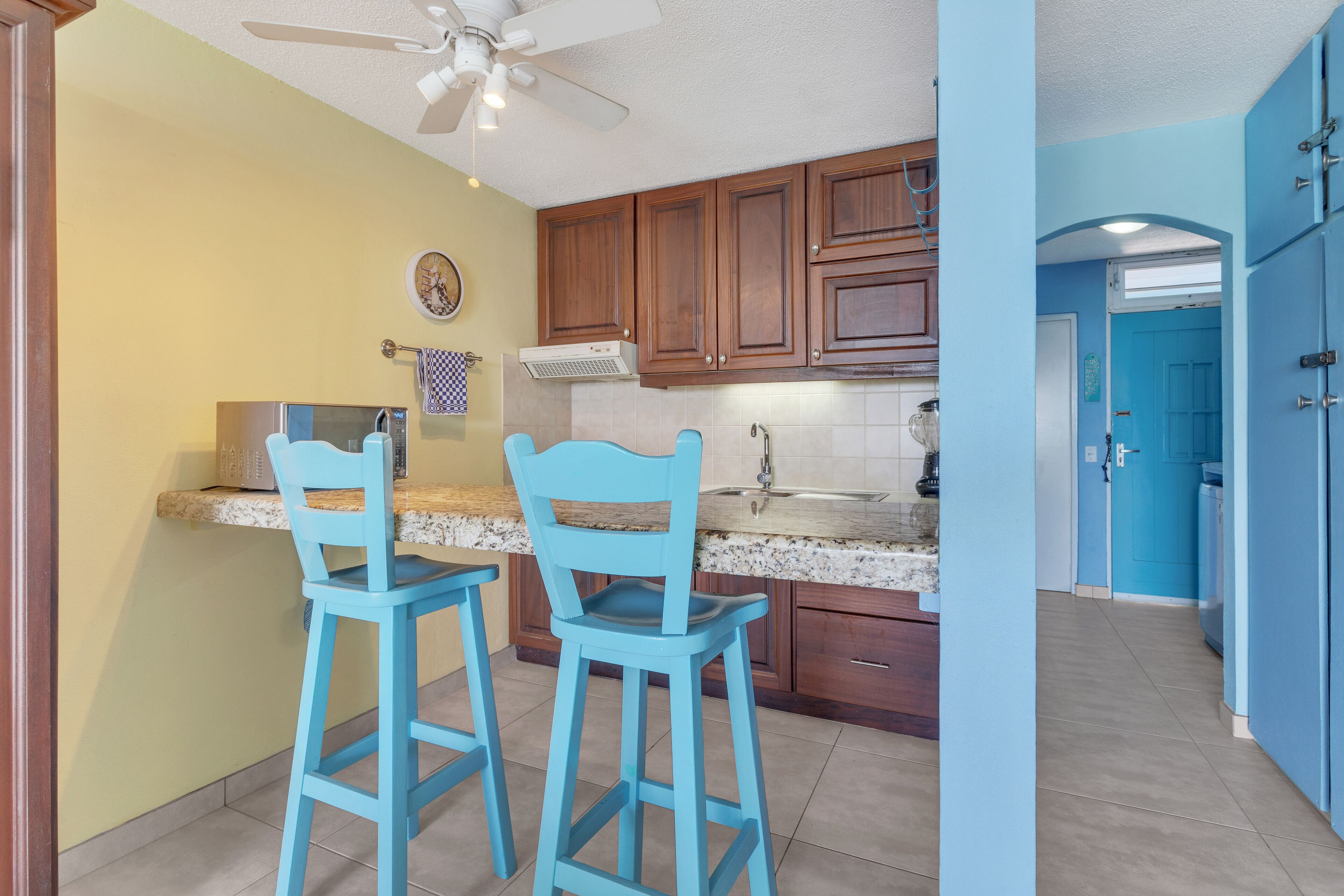 A kitchen with wooden cabinets, a microwave, and two blue bar stools.