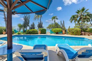 A swimming pool with lounge chairs and palm trees. - Bonaire Oceanfront Apartments (Kralendijk)