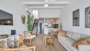 Un'ampia zona giorno con divano, poltrone in vimini, tavolo da pranzo e cucina sullo sfondo.