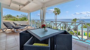Un balcone con vista sul mare, un tavolo con un vaso di fiori e poltrone da relax.