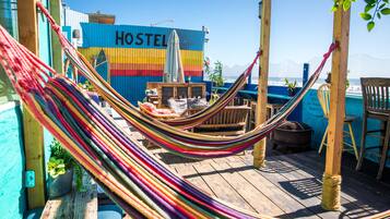 A colorful hammock on a wooden deck with a blue building labeled "HOSTEL" in the background.