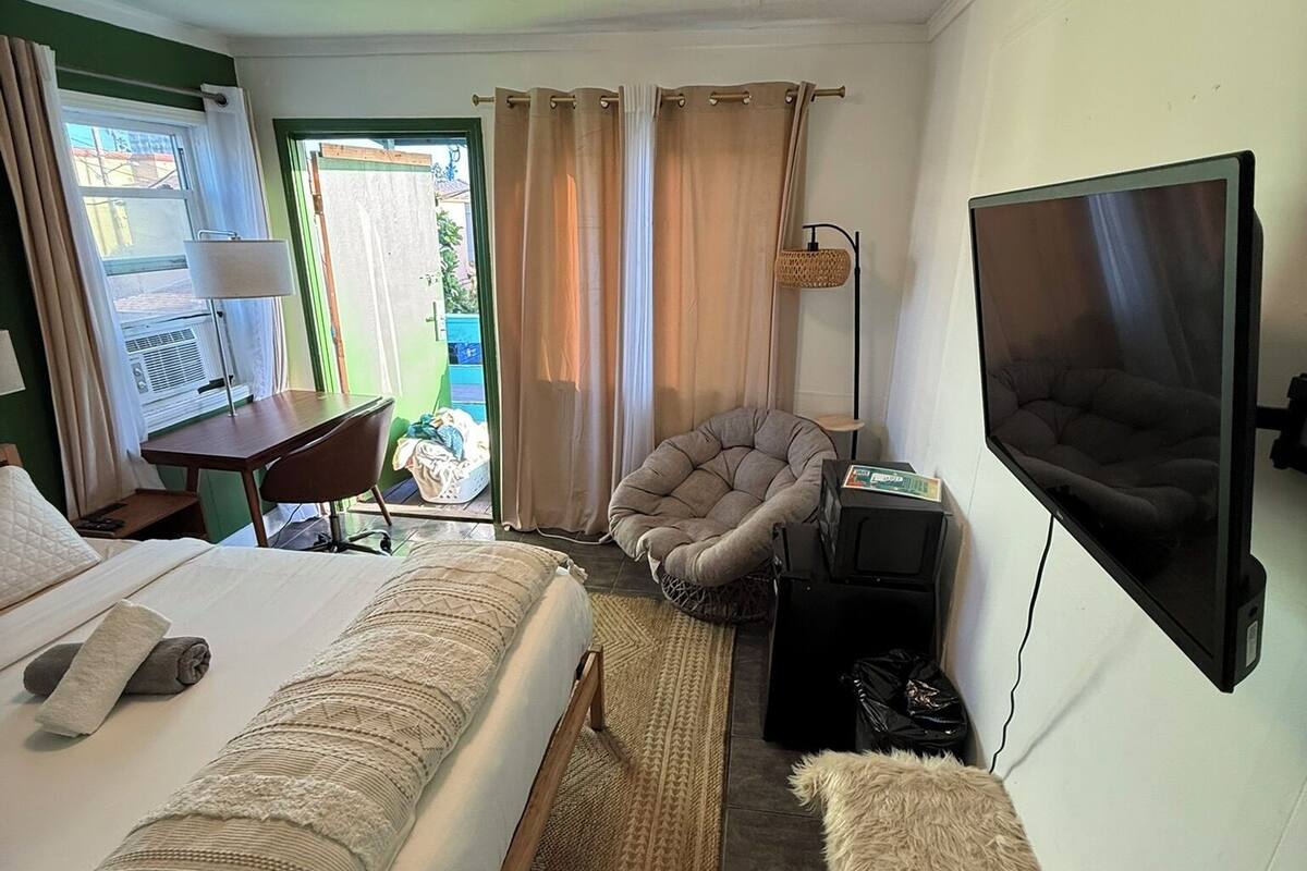 Une chambre d’hôtel avec un lit, une chaise, un bureau, une télévision et une fenêtre avec des rideaux.