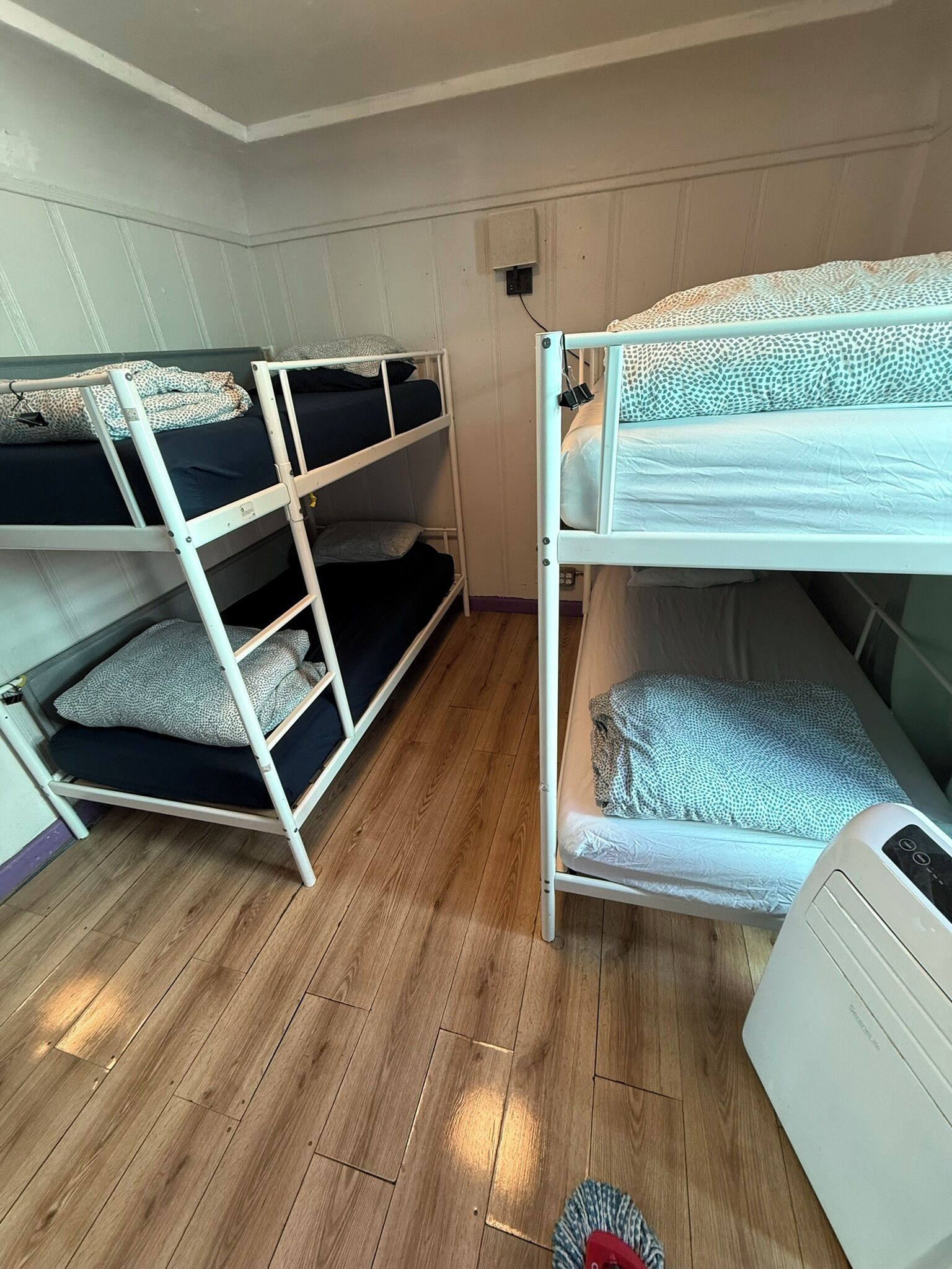 Habitació amb literes, sòl de fusta, radiador blanc i finestra petita.