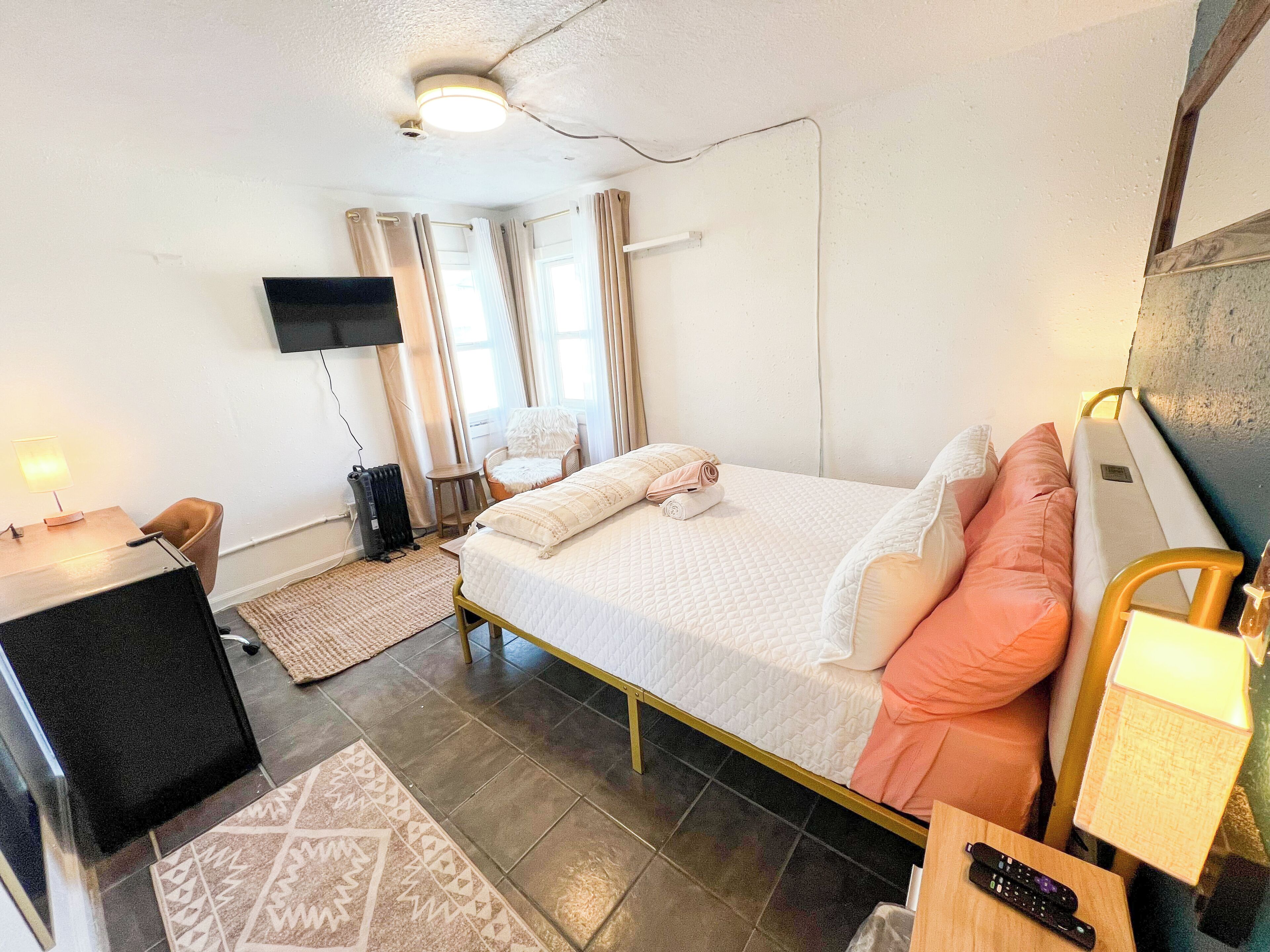 A hotel room with a bed, a desk, a chair, a TV, and a window with curtains.