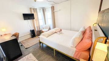 A hotel room with a bed, a desk, a chair, a TV, and a window with curtains.