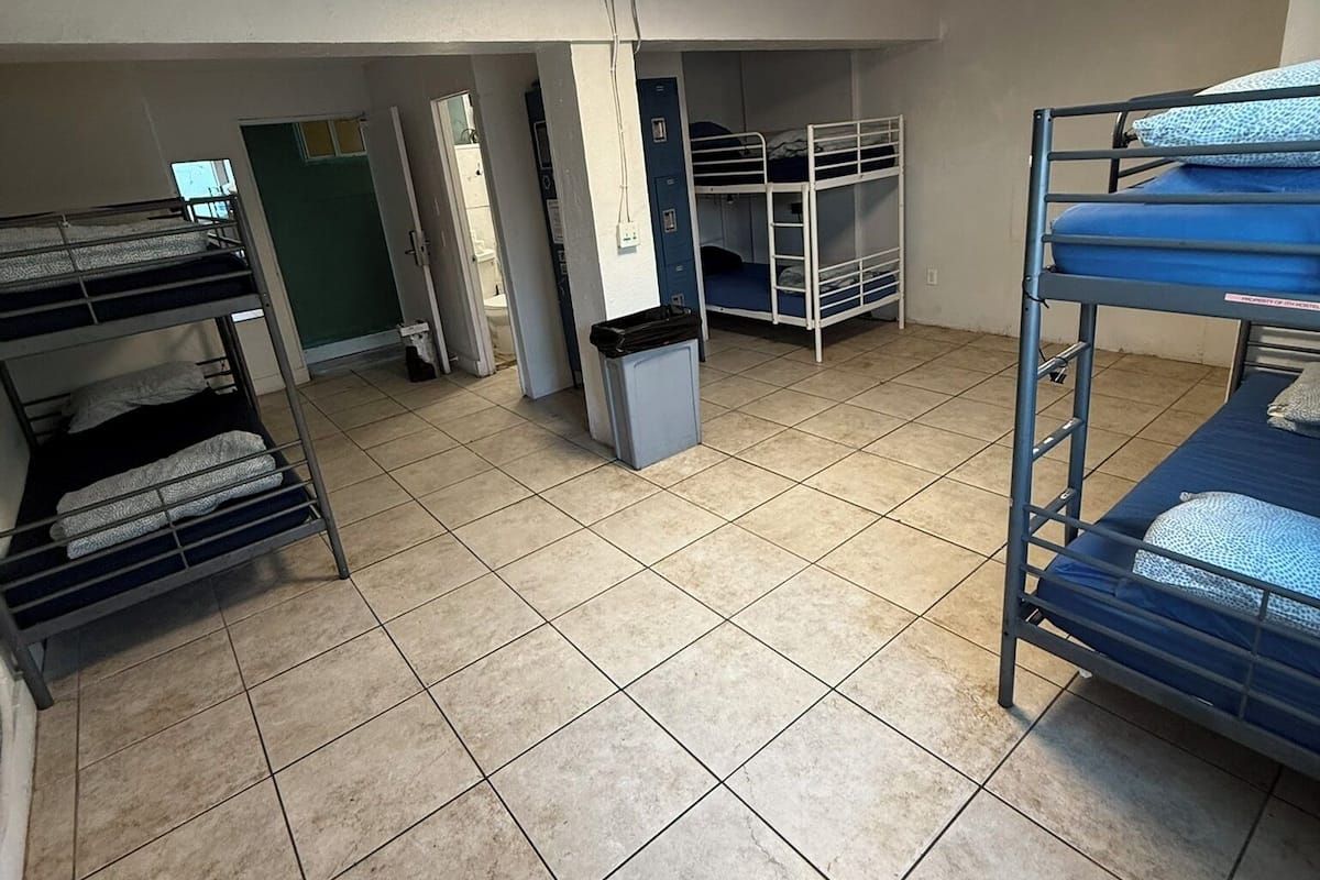 Une chambre de dortoir avec des lits superposés, un sol carrelé et un luminaire au plafond.