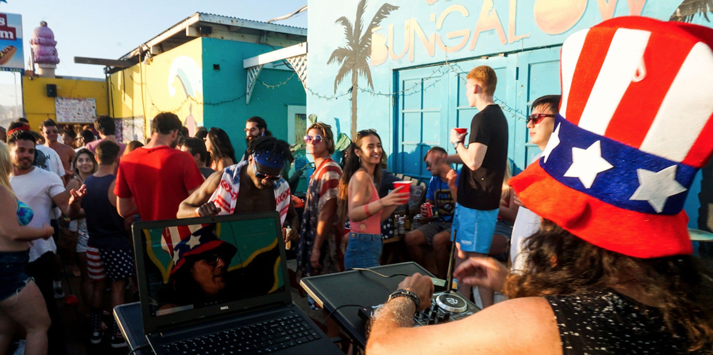 A crowded outdoor event with people, a laptop on a table, and a sign that reads "BUNGAL".
