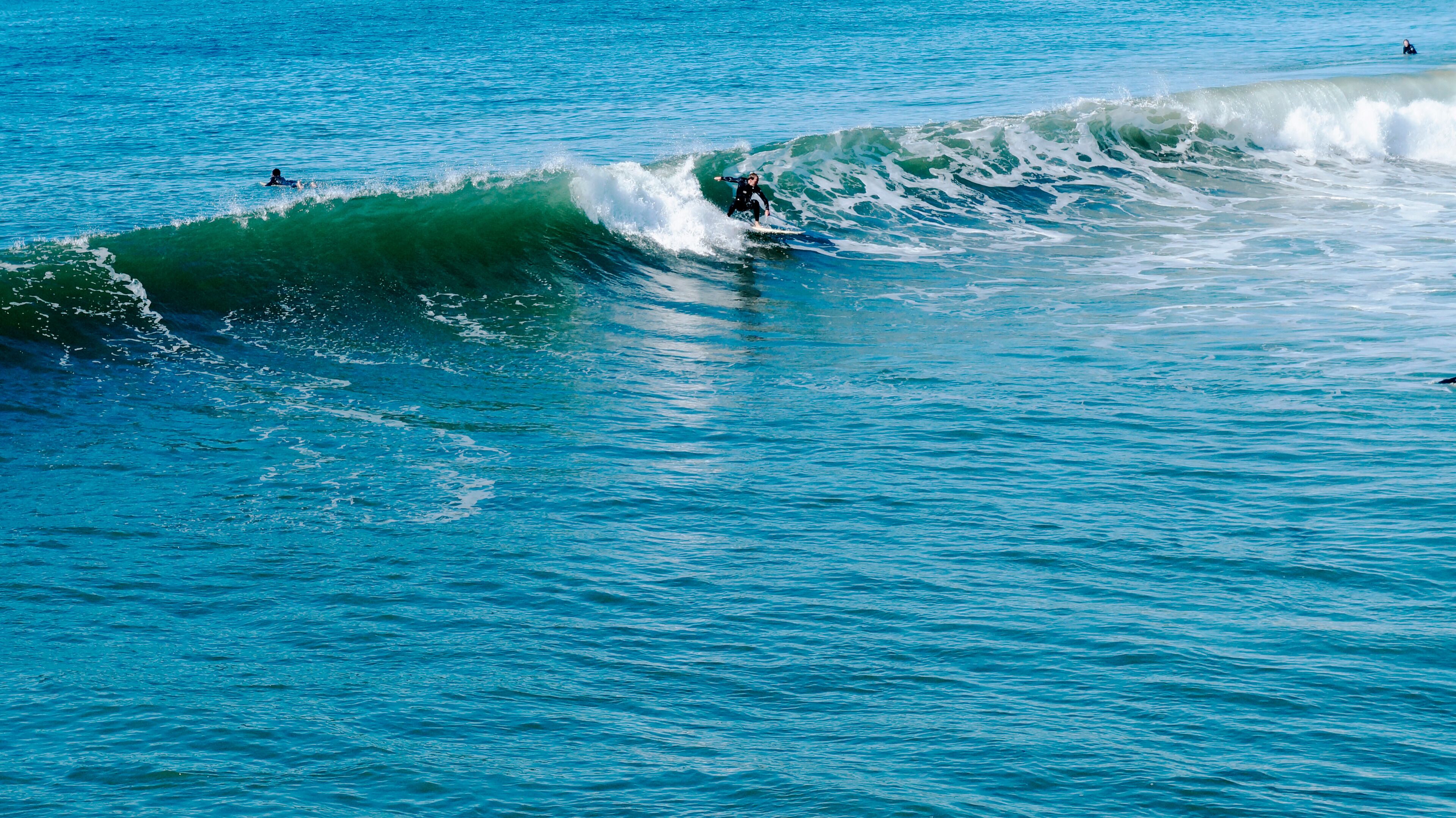 Een helder uitzicht op de oceaan met golven, een surfer die een golf pakt en iemand anders die in het water zwemt.