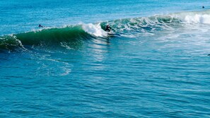 Vista despejada del océano con olas, un surfista montando una ola y otra persona nadando en el agua.
