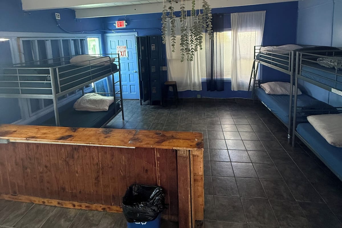 Une chambre de dortoir avec des lits superposés, un banc en bois, une poubelle et un panneau indiquant la sortie.