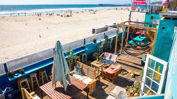 Un restaurante frente a la playa con terraza al aire libre y vistas al océano, con un letrero que dice 'Ocean's Ice Cream'.