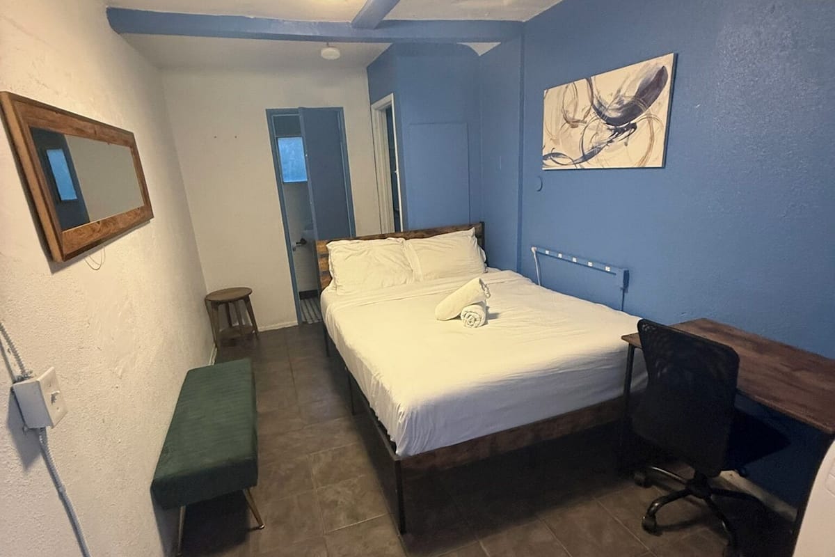 Une chambre à coucher avec un lit, un bureau, une chaise, un banc et un tableau accroché au mur.