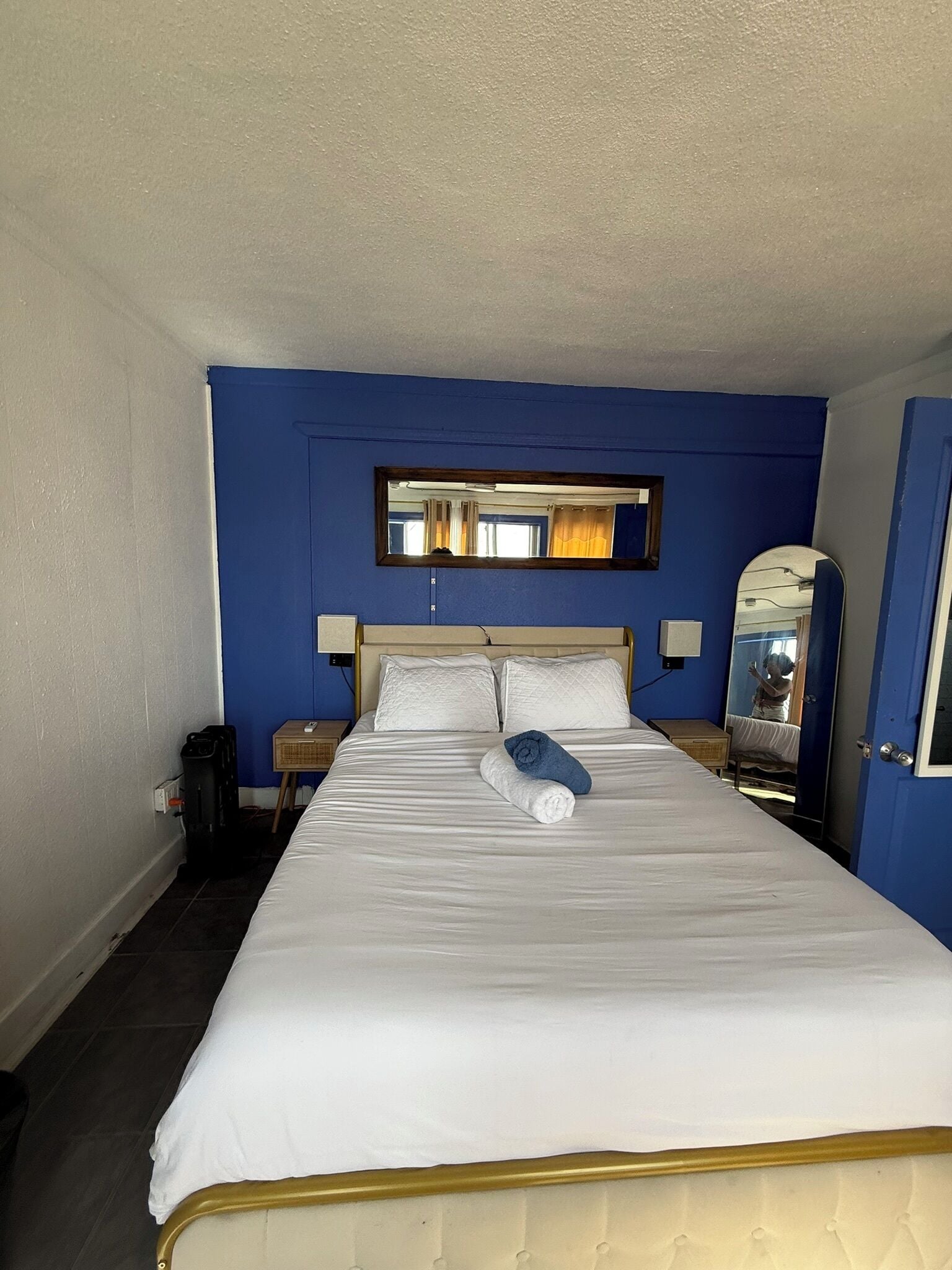 A hotel room with a large bed, two bedside tables, a mirror, and a window with curtains.